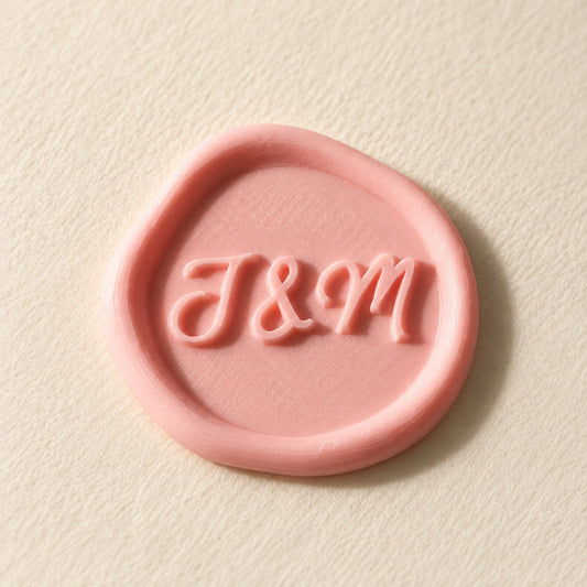 Detalle de un sello adhesivo rosa con iniciales J&M en relieve, acabado rústico