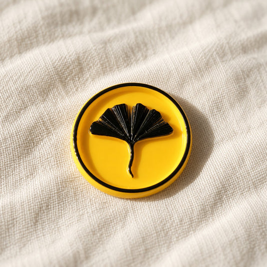 Detalle de un sello adhesivo de hoja de ginkgo negra con borde negro sobre base amarilla, acabado Signature