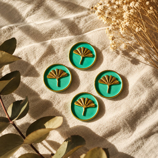 Cuatro sellos adhesivos de ginkgo en dorado sobre base turquesa, acabado Signature, sobre tela crema con eucalipto