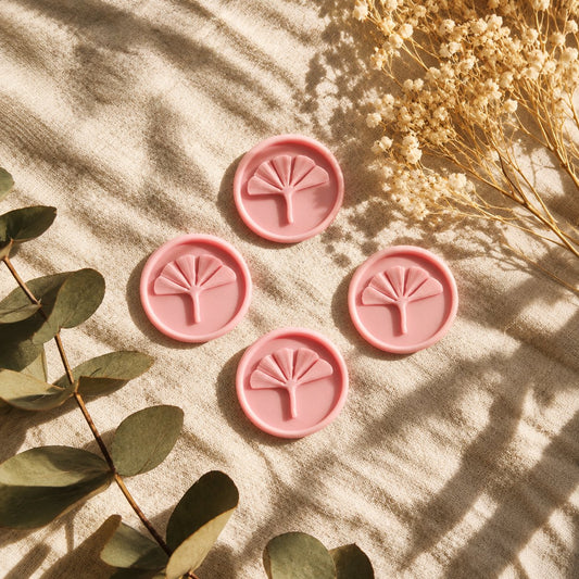 Cuatro sellos adhesivos redondos de ginkgo en relieve color rosa, acabado Minimal, sobre tela crema con eucalipto