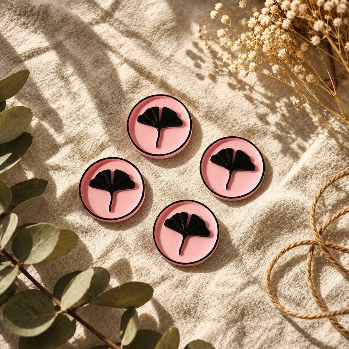 Cuatro sellos adhesivos de ginkgo en negro sobre base rosa, acabado Signature, sobre tela crema con eucalipto