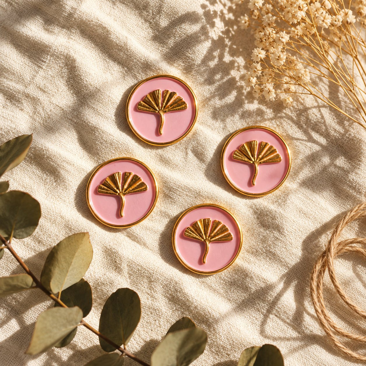 Cuatro sellos adhesivos de ginkgo en dorado sobre base rosa, acabado Signature, sobre tela crema con eucalipto