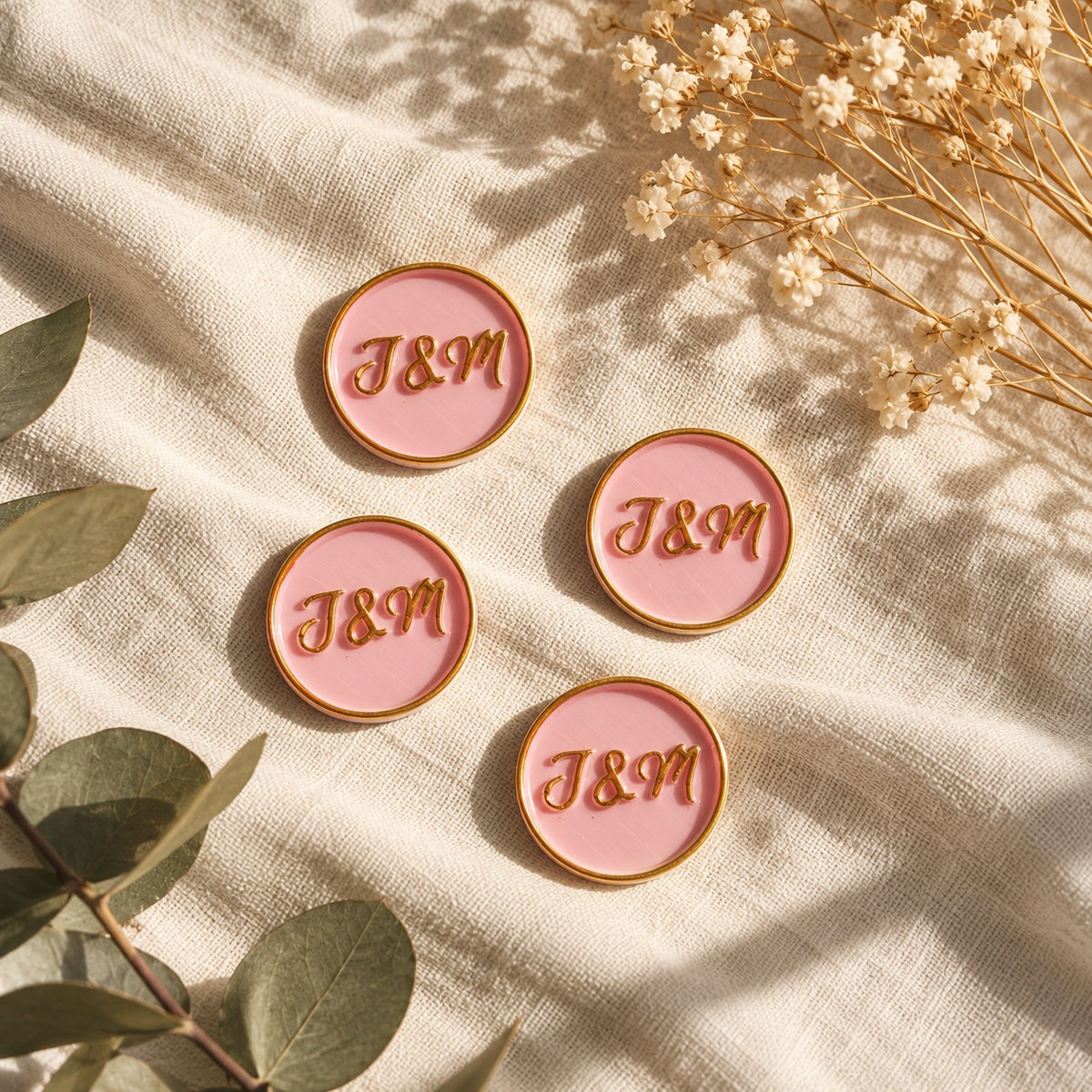 Cinco sellos adhesivos rosa con iniciales en dorado sobre tela crema con eucalipto