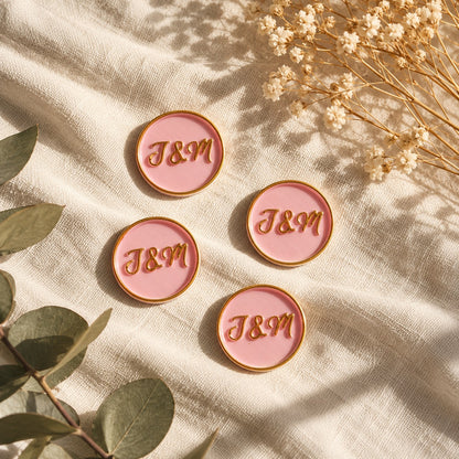 Cinco sellos adhesivos rosa con iniciales en dorado sobre tela crema con eucalipto