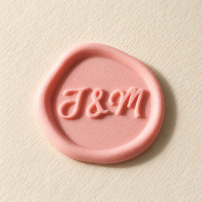 Detalle de un sello adhesivo rosa con iniciales J&M en relieve, acabado rústico