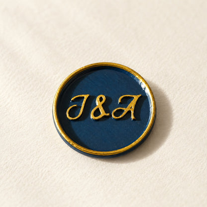 Detalle de un sello adhesivo azul marino con iniciales y borde dorado pintado a mano