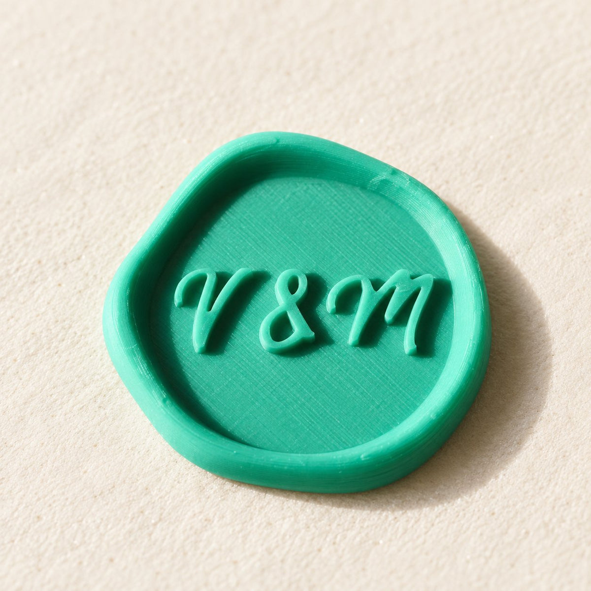 Detalle de un sello adhesivo turquesa con iniciales V&M en relieve, acabado rústico