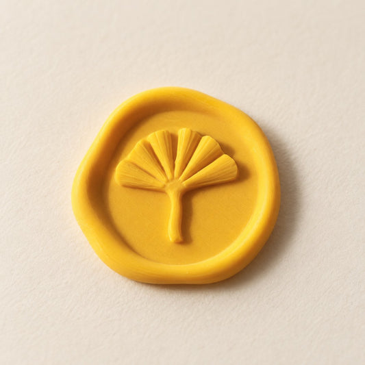 Detalle de un sello adhesivo amarillo con hoja de ginkgo en relieve, acabado rústico de borde irregular