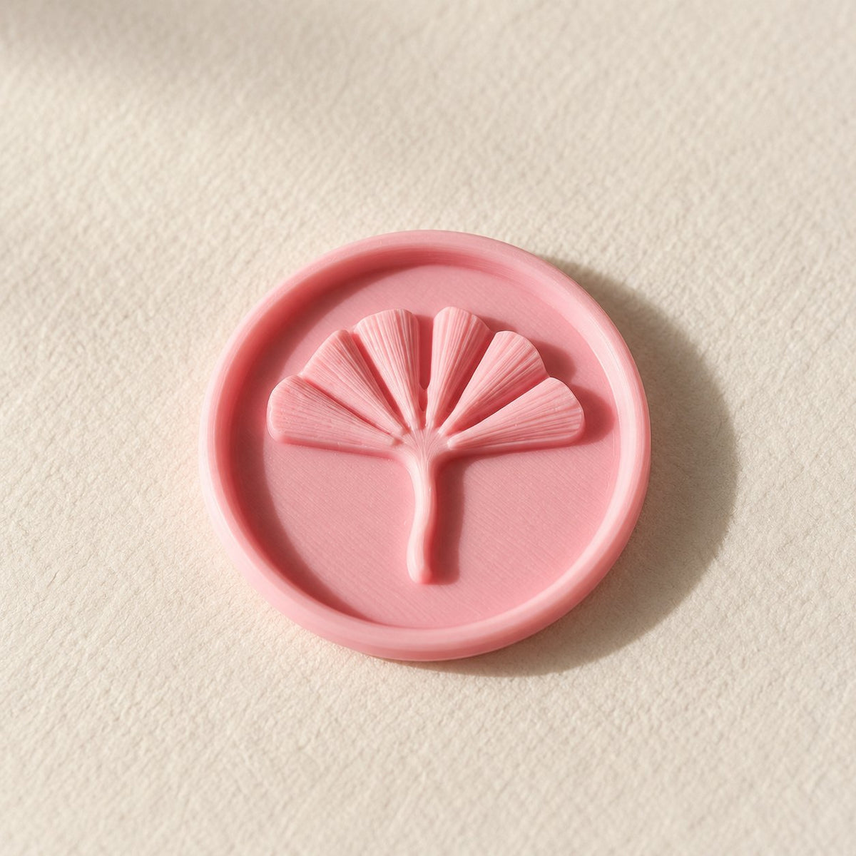 Detalle de un sello adhesivo redondo rosa con hoja de ginkgo en relieve, acabado Minimal