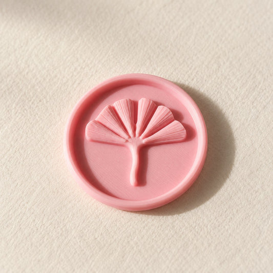 Detalle de un sello adhesivo redondo rosa con hoja de ginkgo en relieve, acabado Minimal