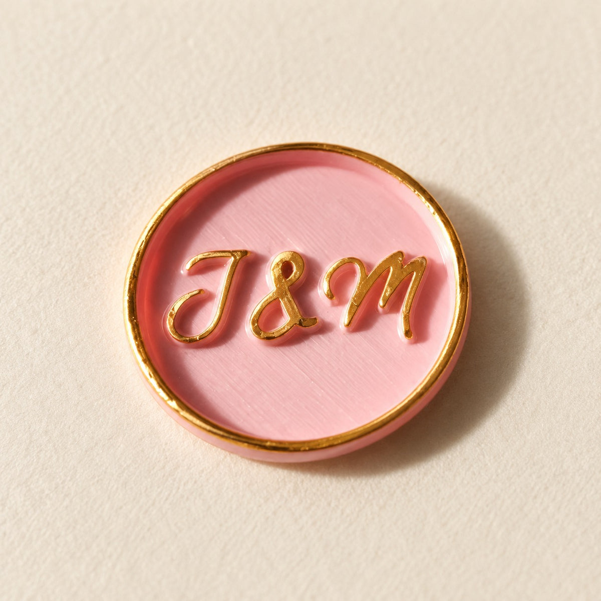 Detalle de un sello adhesivo rosa con iniciales y borde dorado pintado a mano