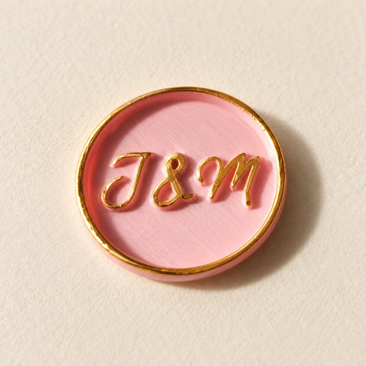 Detalle de un sello adhesivo rosa con iniciales y borde dorado pintado a mano