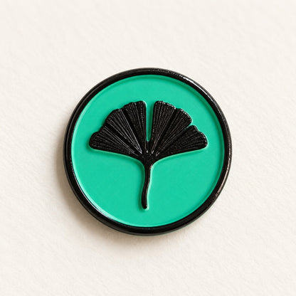 Detalle de un sello adhesivo de hoja de ginkgo negra con borde negro sobre base turquesa, acabado Signature