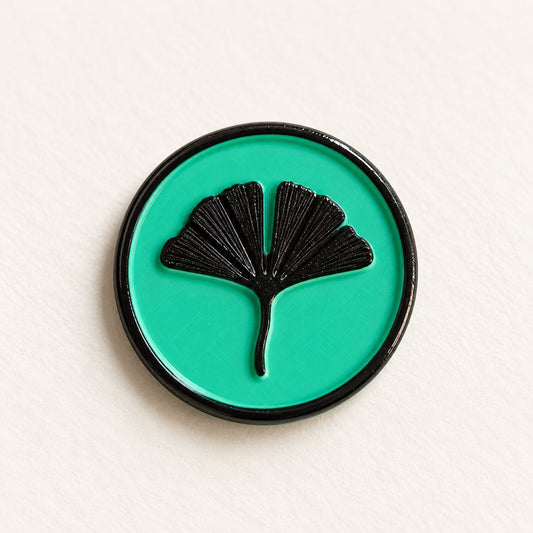 Detalle de un sello adhesivo de hoja de ginkgo negra con borde negro sobre base turquesa, acabado Signature