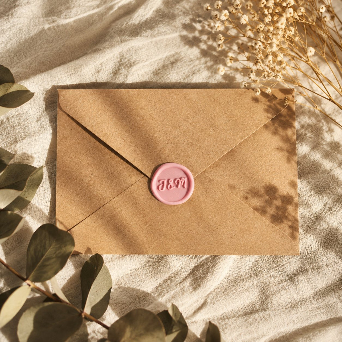 Sello adhesivo rosa con iniciales en relieve sobre un sobre kraft