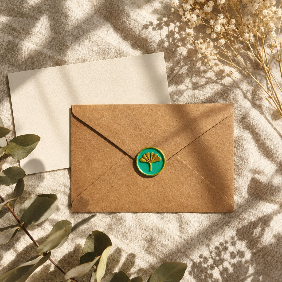 Sello adhesivo de ginkgo dorado y turquesa sobre un sobre kraft con tarjeta crema