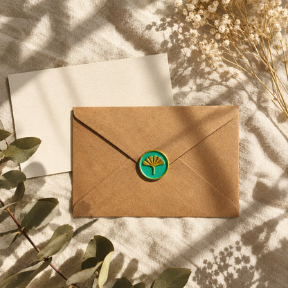 Sello adhesivo de ginkgo dorado y turquesa sobre un sobre kraft con tarjeta crema