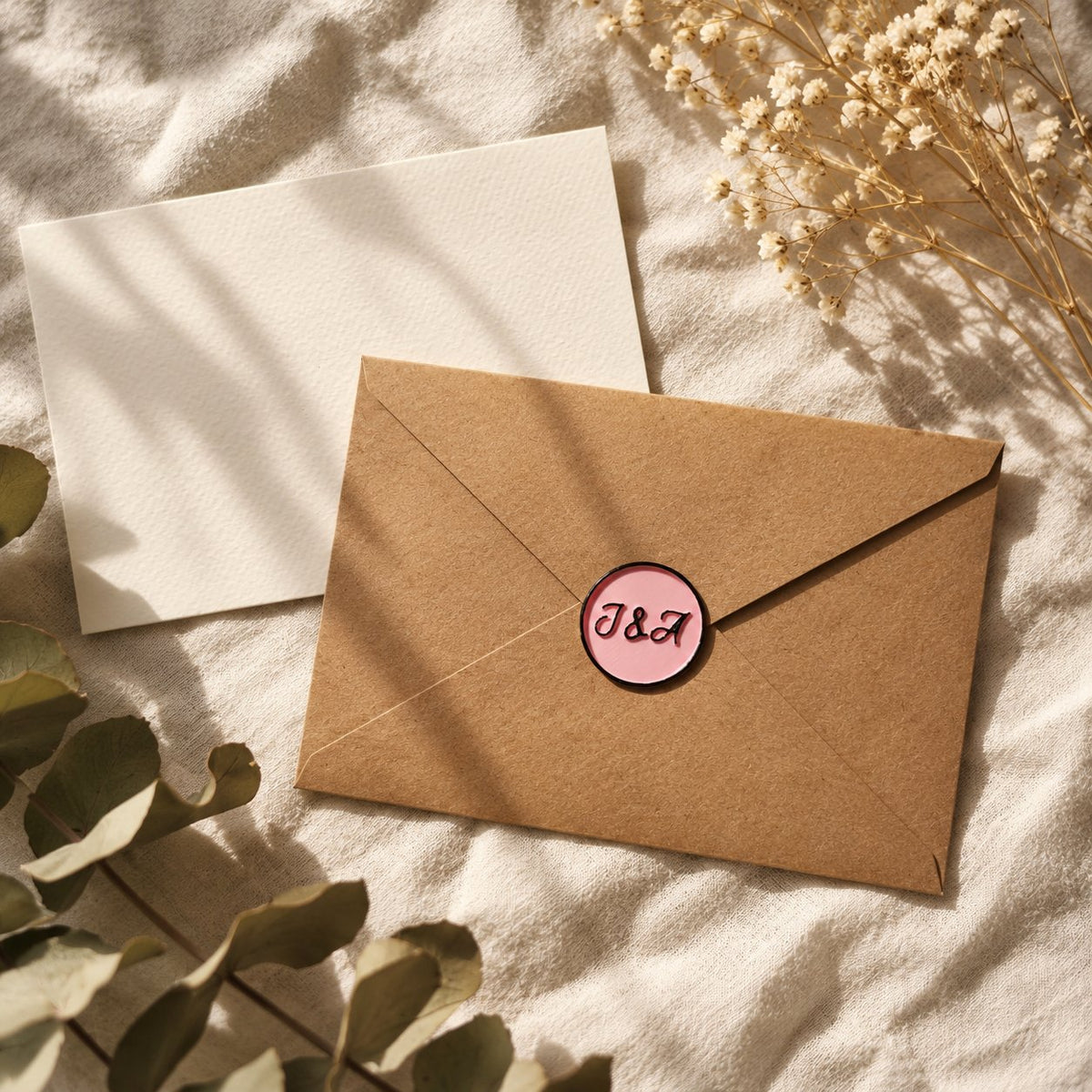 Sello adhesivo rosa con iniciales en negro sobre un sobre kraft con tarjeta crema