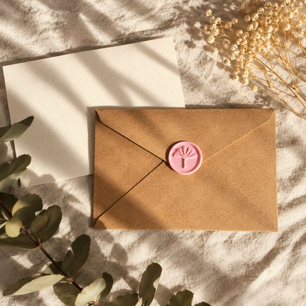 Sello adhesivo de ginkgo rosa sobre un sobre kraft con tarjeta crema