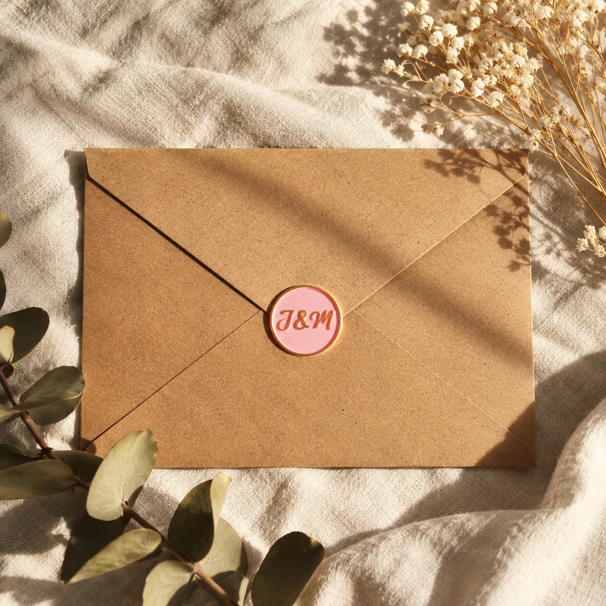 Sello adhesivo rosa con iniciales sobre un sobre kraft