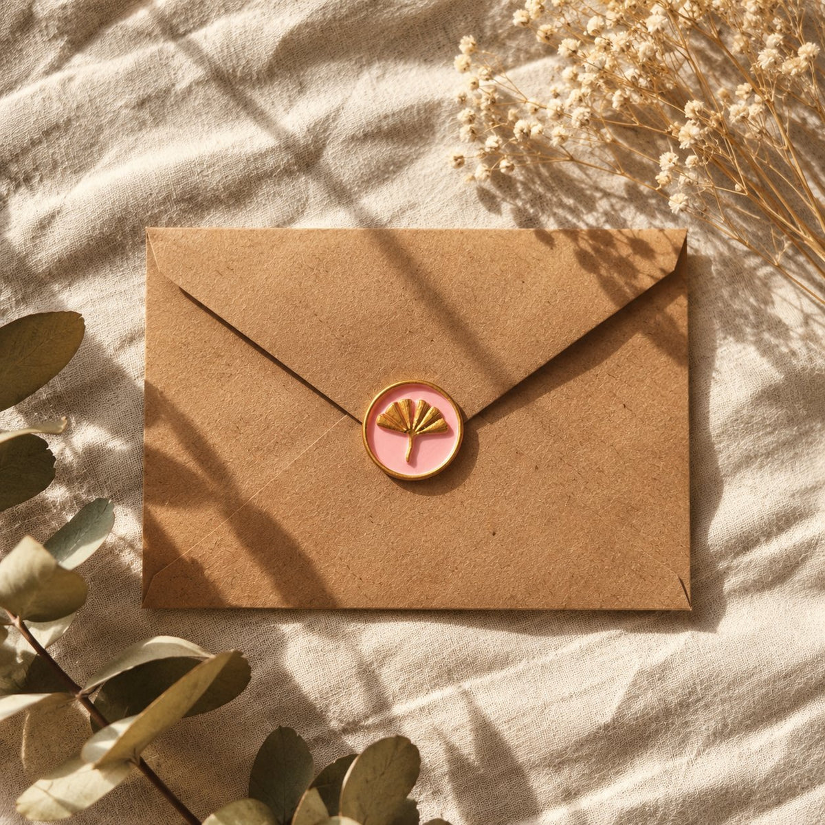 Sello adhesivo de ginkgo dorado y rosa sobre un sobre kraft