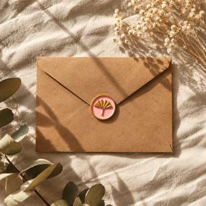 Sello adhesivo de ginkgo dorado y rosa sobre un sobre kraft