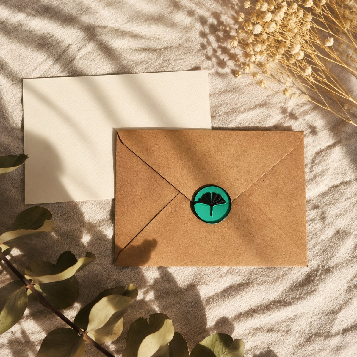 Sello adhesivo de ginkgo negro y turquesa sobre un sobre kraft con tarjeta crema