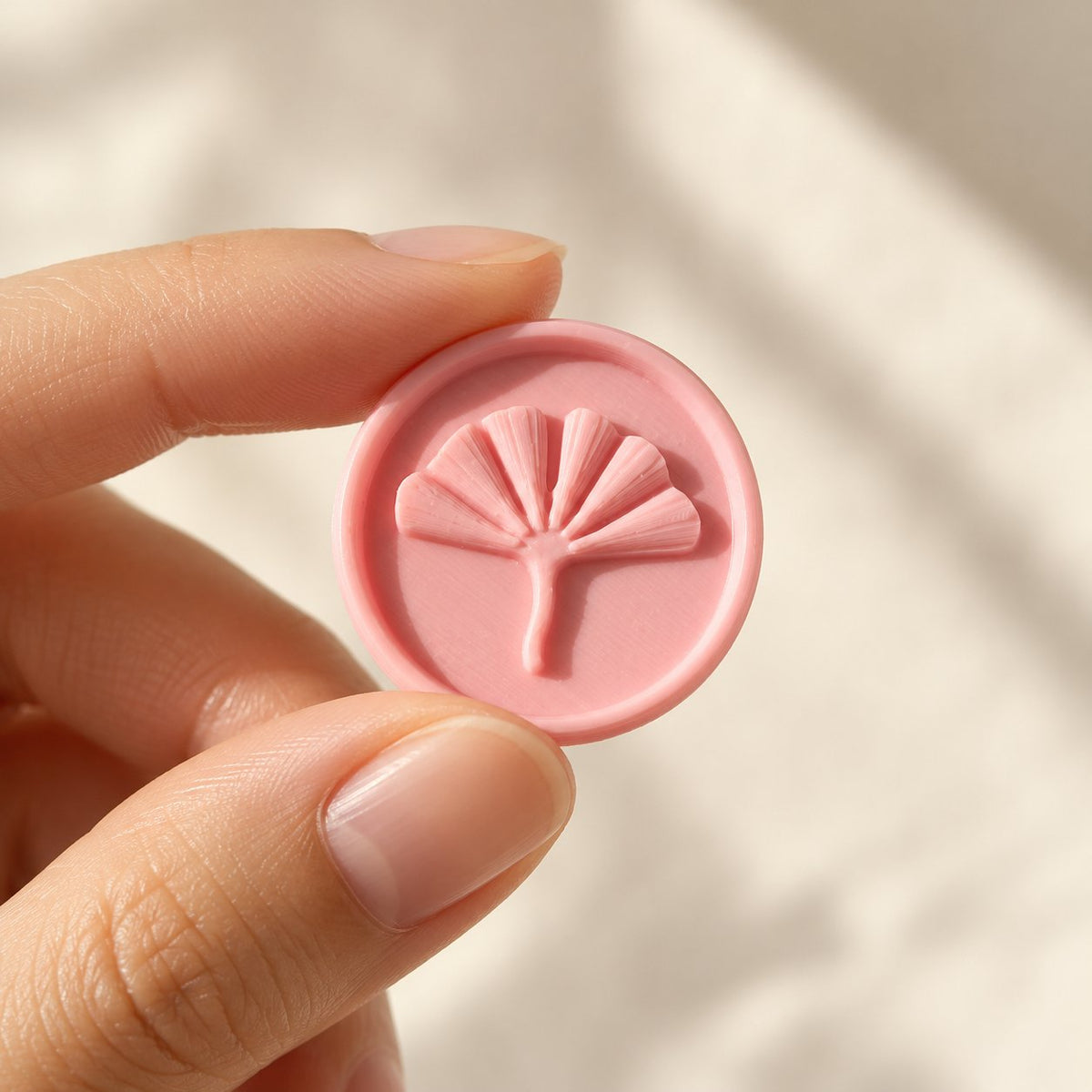 Mano sujetando un sello adhesivo redondo de ginkgo rosa, acabado Minimal