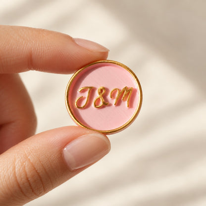 Mano sujetando un sello adhesivo rosa con iniciales y borde dorado