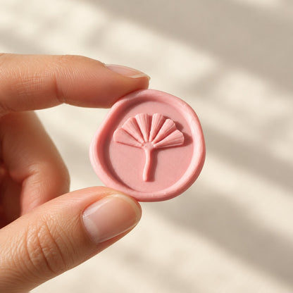 Mano sujetando un sello adhesivo de ginkgo en rosa con borde rústico