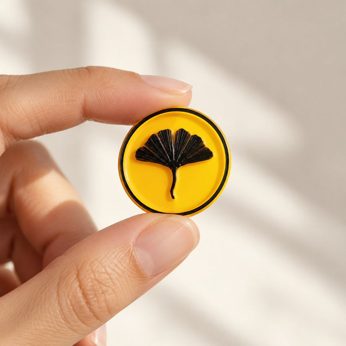 Mano sujetando un sello adhesivo de ginkgo negro sobre base amarilla, acabado Signature