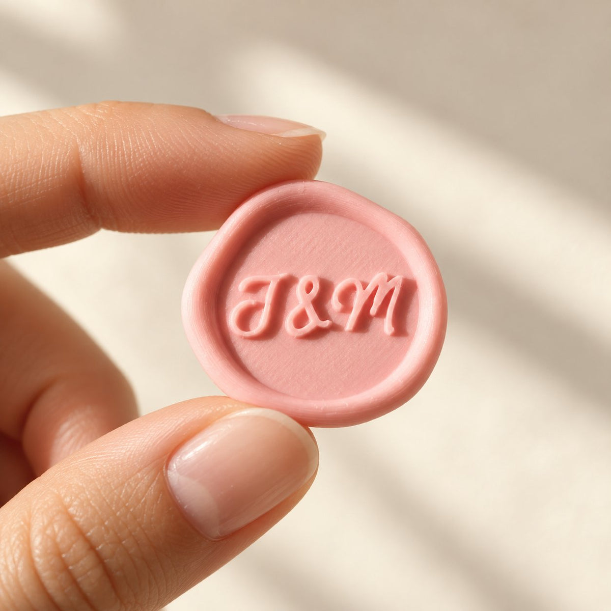 Mano sujetando un sello adhesivo rosa con iniciales en relieve, acabado rústico