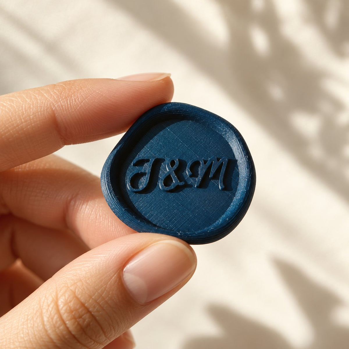 Mano sujetando un sello adhesivo azul marino con iniciales en relieve, acabado rústico