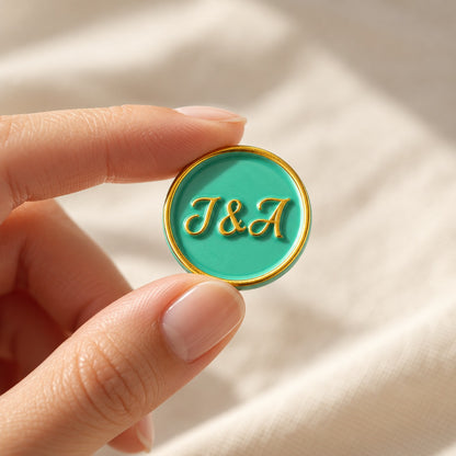 Mano sujetando un sello adhesivo turquesa con iniciales y borde dorado