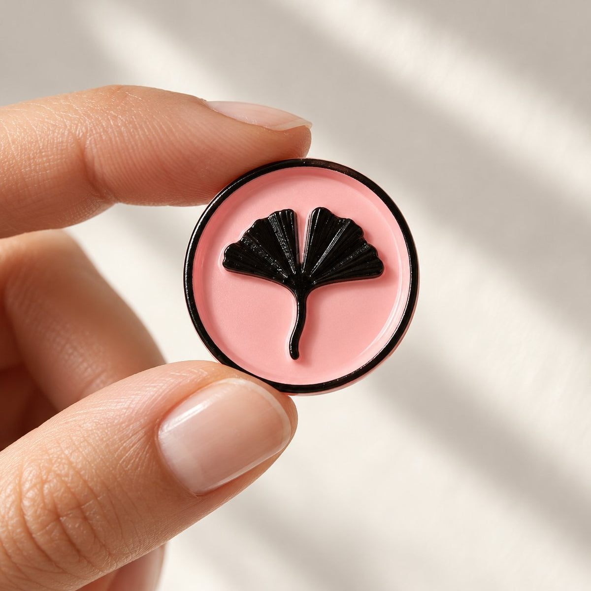 Mano sujetando un sello adhesivo rosa con hoja de ginkgo en negro